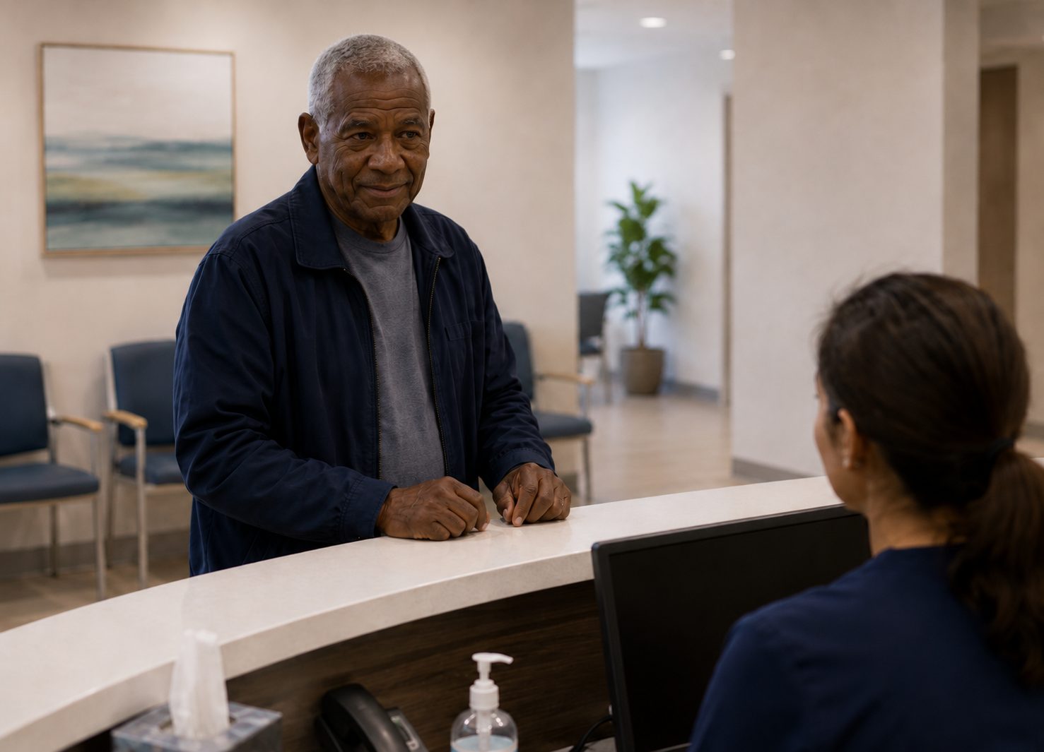 An elderly patient standing at the admission desk talking with a staff member